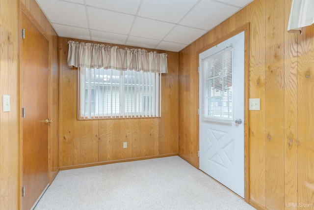 interior space featuring carpet, wood walls, baseboards, and a drop ceiling