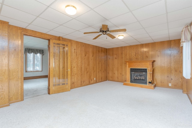 unfurnished living room with ceiling fan, wood walls, and carpet floors