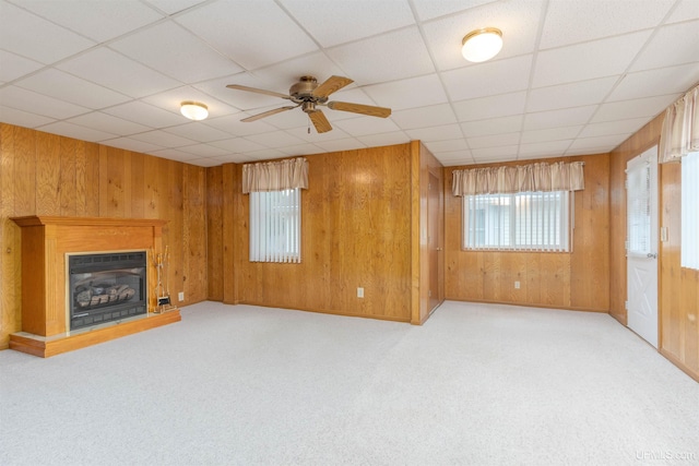 unfurnished living room with wood walls, a wealth of natural light, a ceiling fan, and a glass covered fireplace