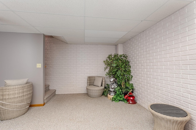 sitting room featuring a paneled ceiling, brick wall, and carpet