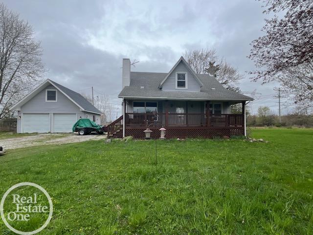 rear view of house with a lawn, a chimney, driveway, a detached garage, and a porch