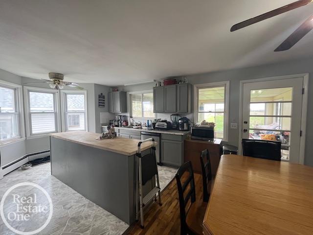 kitchen with a ceiling fan, a sink, baseboard heating, gray cabinetry, and a kitchen island