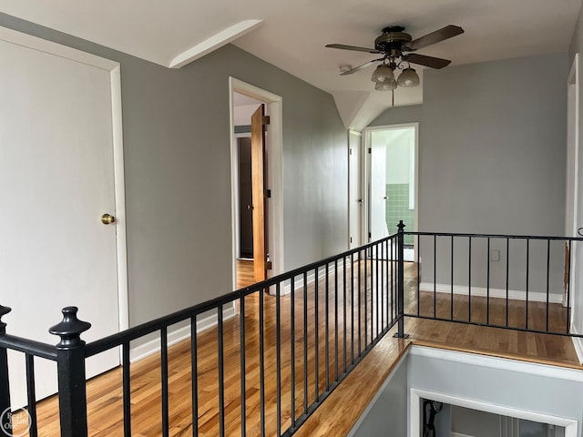 corridor featuring baseboards, an upstairs landing, and wood finished floors