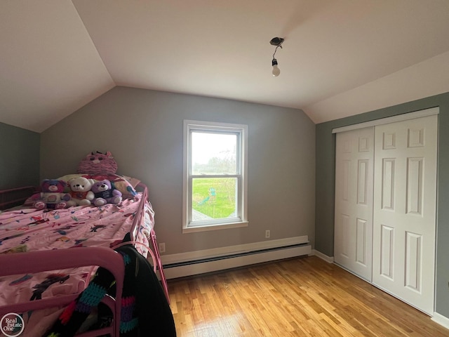 bedroom with a closet, vaulted ceiling, light wood-style flooring, and baseboard heating