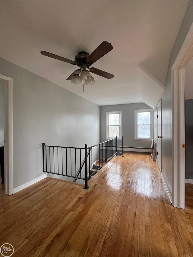 additional living space with wood finished floors, a ceiling fan, baseboards, a baseboard heating unit, and lofted ceiling