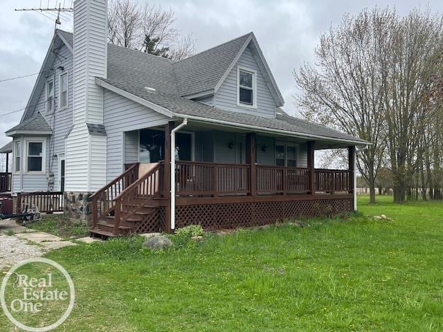 view of front facade with a chimney, a front yard, roof with shingles, and covered porch