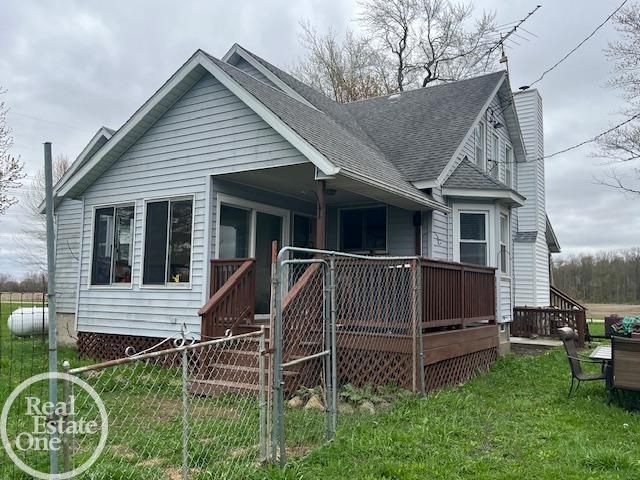 view of front facade featuring a chimney, a deck, fence, a shingled roof, and a front yard