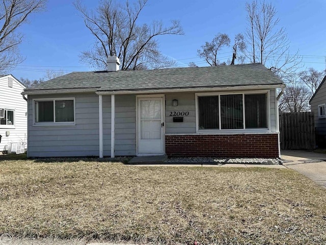 view of front of property featuring fence, brick siding, a front lawn, a chimney, and a shingled roof