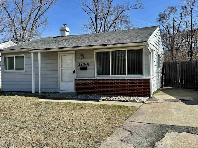 view of front of property with brick siding, fence, roof with shingles, and a chimney