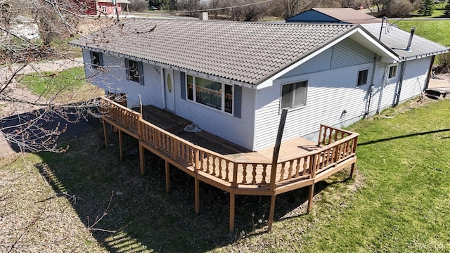 rear view of property with a lawn, a deck, and a tiled roof