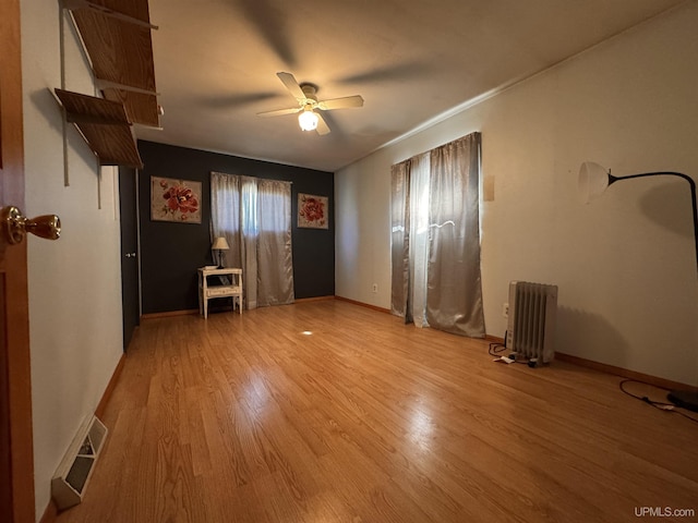 unfurnished bedroom with baseboards, radiator, visible vents, and wood finished floors