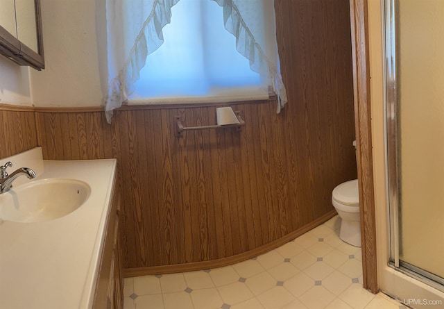 bathroom with toilet, a shower with door, wood walls, wainscoting, and vanity