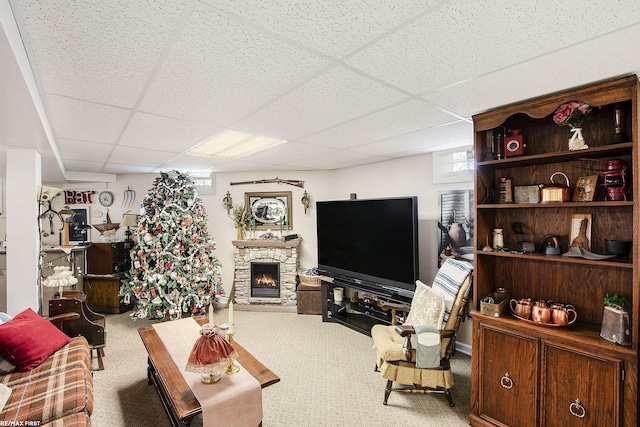 carpeted living area with a stone fireplace and a paneled ceiling
