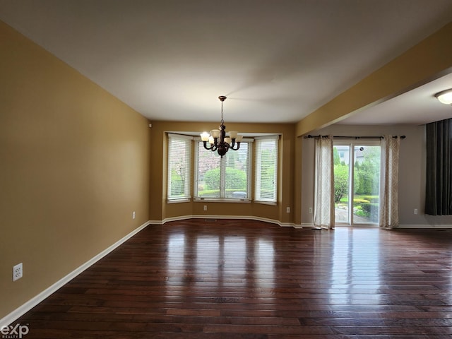 empty room with a notable chandelier, dark wood-type flooring, and baseboards