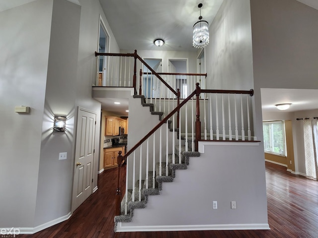 staircase featuring a high ceiling, baseboards, a notable chandelier, and wood finished floors