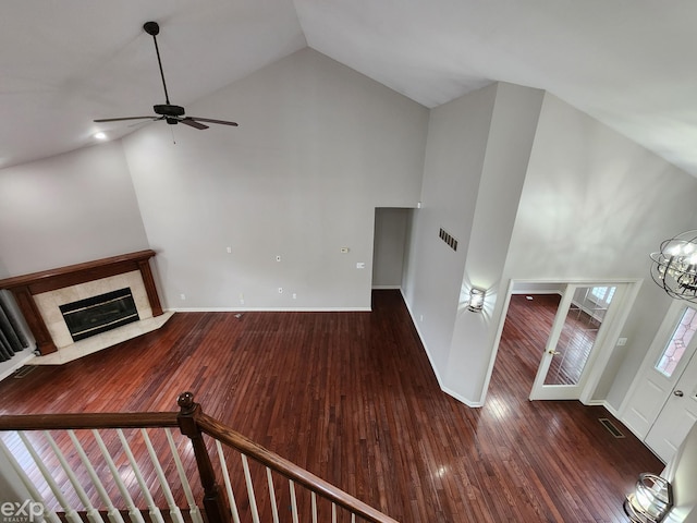 unfurnished living room with baseboards, wood-type flooring, ceiling fan with notable chandelier, a fireplace with flush hearth, and high vaulted ceiling