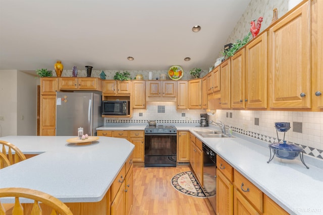 kitchen with light wood finished floors, a sink, backsplash, black appliances, and light countertops