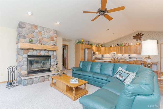 living area with lofted ceiling, a stone fireplace, light carpet, and a ceiling fan