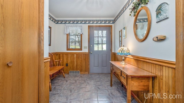 doorway featuring wooden walls, wainscoting, and visible vents