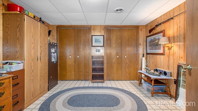 interior space featuring freestanding refrigerator, a paneled ceiling, visible vents, a barn door, and wooden walls