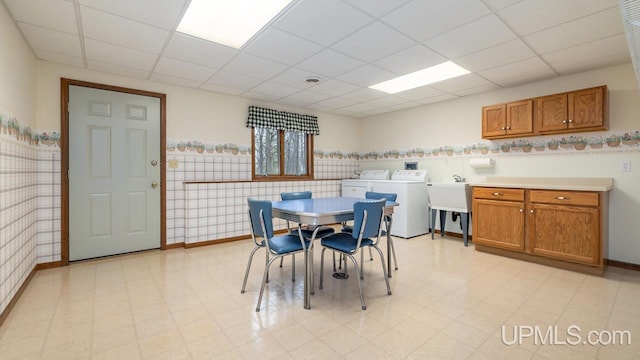 dining space featuring baseboards, a drop ceiling, washer and dryer, and light floors