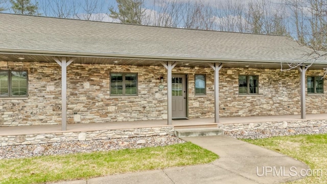 entrance to property with stone siding, a porch, and roof with shingles