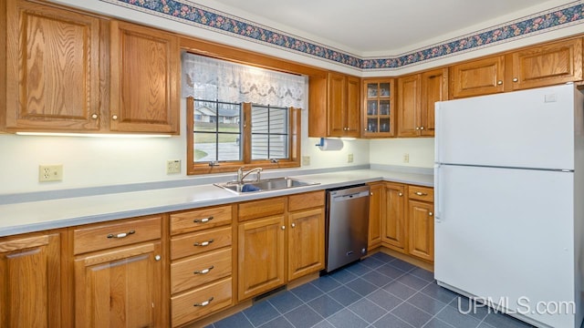kitchen featuring brown cabinets, a sink, freestanding refrigerator, dark tile patterned flooring, and dishwasher