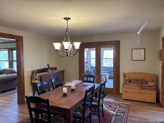 dining area with french doors, light wood-style flooring, and a chandelier