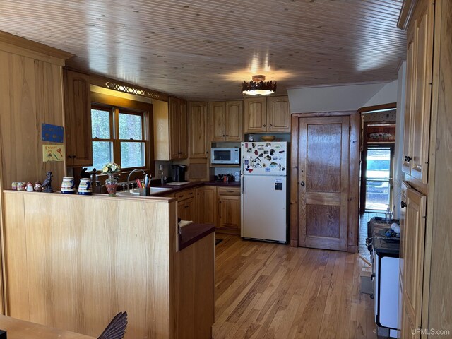 kitchen with white appliances, a sink, light wood-style floors, a peninsula, and dark countertops