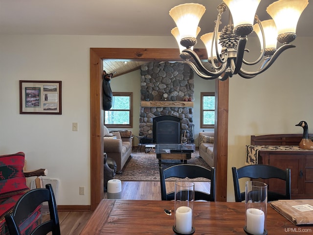 dining room featuring wood finished floors, healthy amount of natural light, vaulted ceiling, baseboards, and a stone fireplace