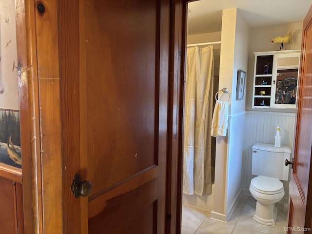 bathroom with tile patterned flooring, toilet, wainscoting, and a shower with curtain