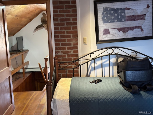 bedroom with a baseboard heating unit, wood finished floors, vaulted ceiling, and a desk