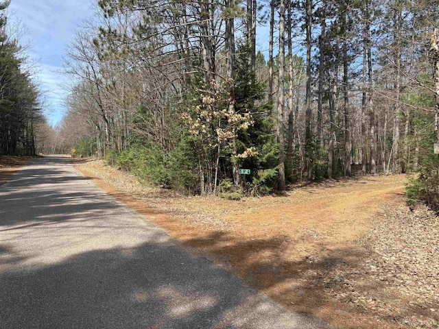 view of asphalt street featuring a wooded view