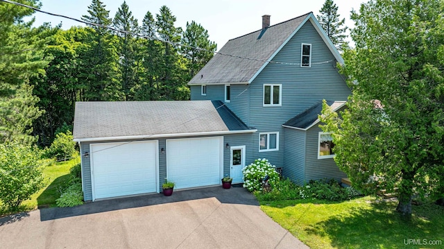 view of front facade with a shingled roof, a front yard, a chimney, and a garage