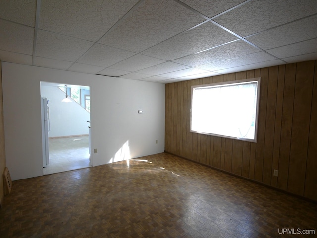 unfurnished room with a drop ceiling, wooden walls, and parquet floors
