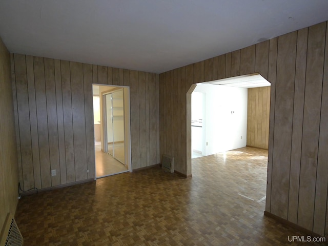 spare room with wooden walls, visible vents, and arched walkways