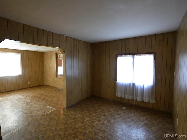 spare room featuring wood walls, a wealth of natural light, and arched walkways