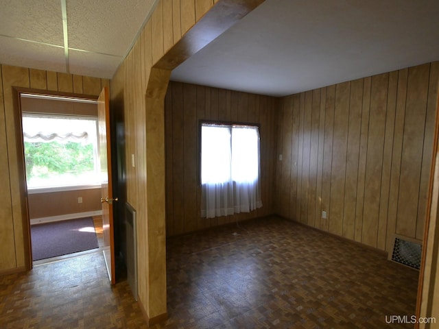 unfurnished room with wood walls, baseboards, and arched walkways