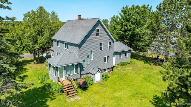 back of house with a chimney, roof with shingles, and a lawn