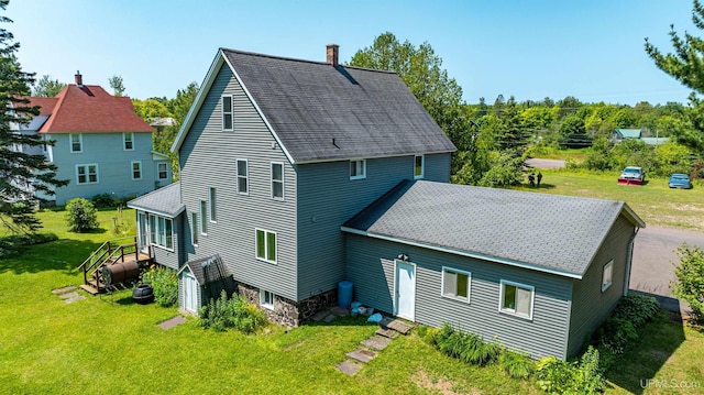 back of property featuring heating fuel, a shingled roof, a yard, and a chimney