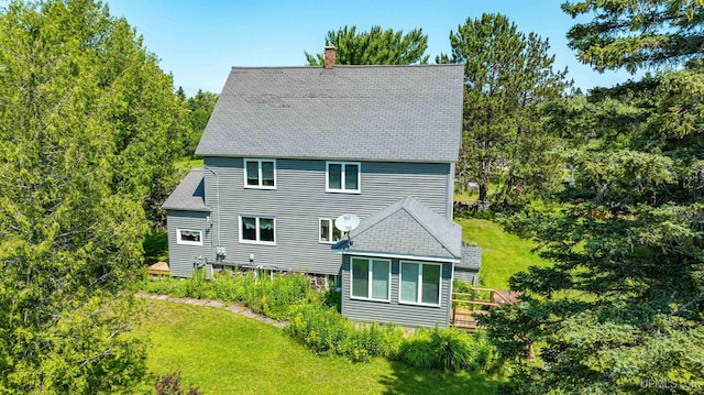 back of property featuring a chimney, a shingled roof, and a lawn