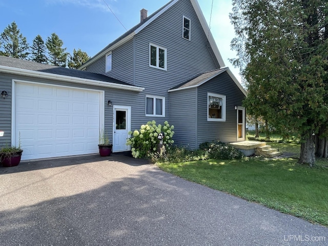 view of front of home featuring a chimney, a front lawn, aphalt driveway, and a garage