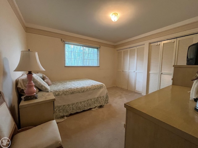 bedroom with light colored carpet, crown molding, and two closets
