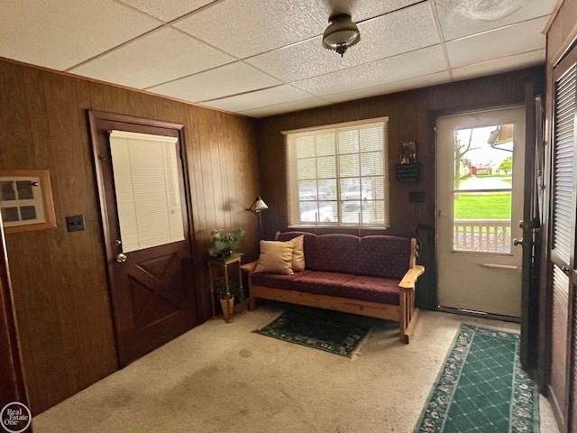 living area with a paneled ceiling, wood walls, and carpet