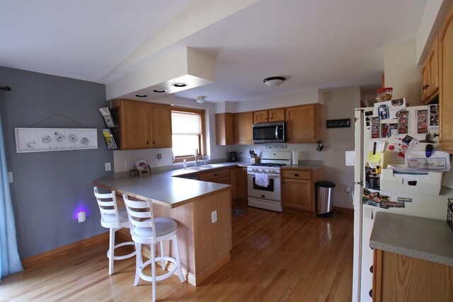 kitchen featuring white appliances, a peninsula, a kitchen breakfast bar, light wood-style floors, and vaulted ceiling