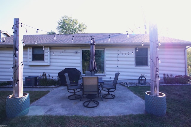 back of property with a patio, cooling unit, a shingled roof, and a lawn