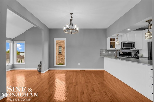 kitchen featuring light wood-style flooring, stainless steel appliances, white cabinets, a chandelier, and tasteful backsplash