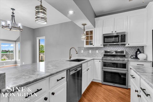kitchen with an inviting chandelier, a sink, white cabinetry, appliances with stainless steel finishes, and light stone counters