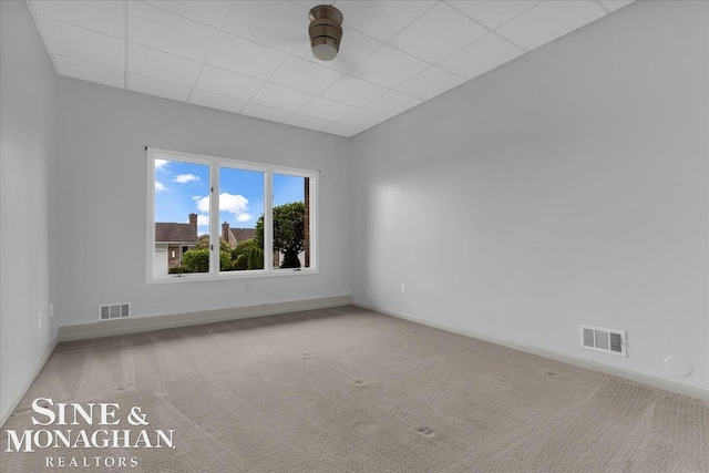 empty room with a drop ceiling, visible vents, baseboards, and carpet floors