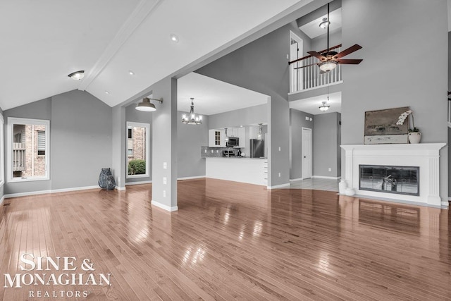 unfurnished living room with baseboards, wood finished floors, ceiling fan with notable chandelier, and a glass covered fireplace